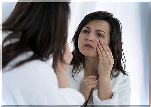 The woman is looking at her face in the mirror